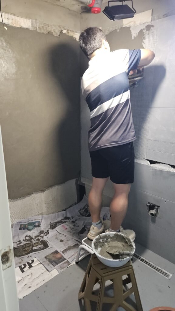 발판 위에 올라서서 벽면 상단까지 폴리머 몰탈을 미장하는 모습
