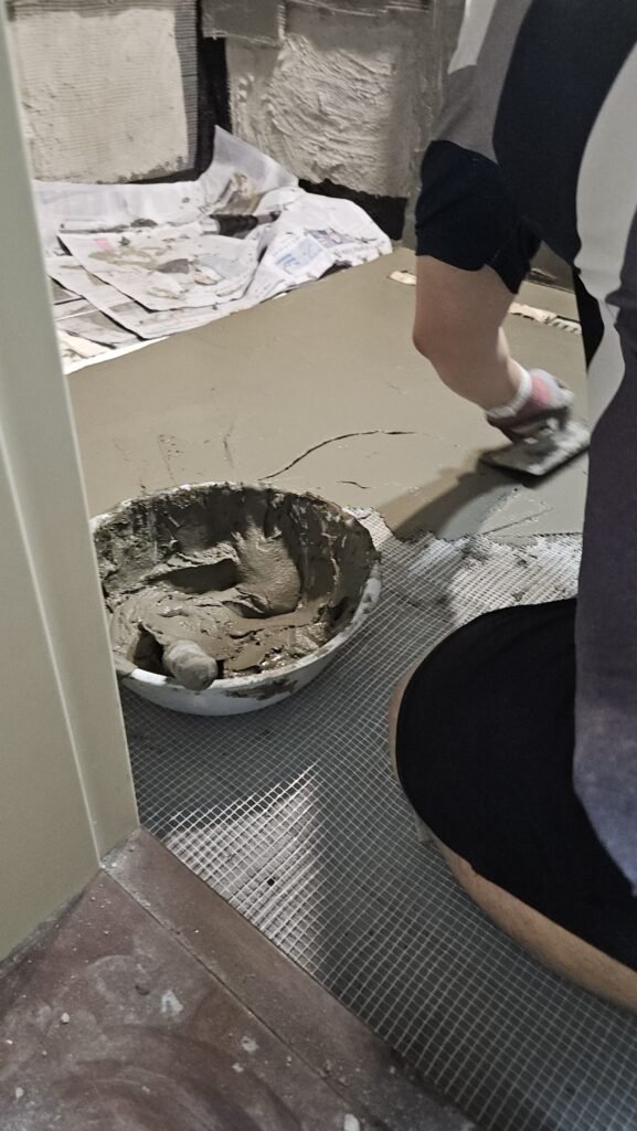 욕실 바닥에 유리섬유 메쉬를 깔고 그 위에 폴리머 몰탈을 미장하는 모습